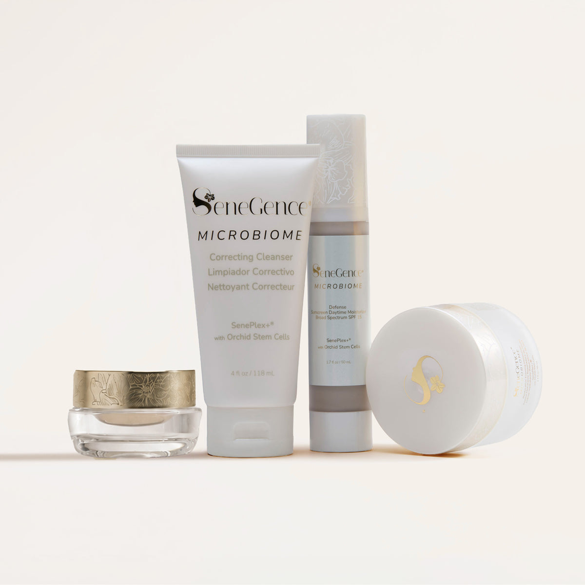 Microbiome Defense Daytime Moisturizer SPF 15 by SeneGence: the Microbiome SkinCare Regimen Set together, with EyeCrème in a small clear jar under a gold orchid lid, the white Microbiome Correcting Cleanser tube, the pump bottle and the Microbiome Restorative Evening Moisturizer jar resting on its side.