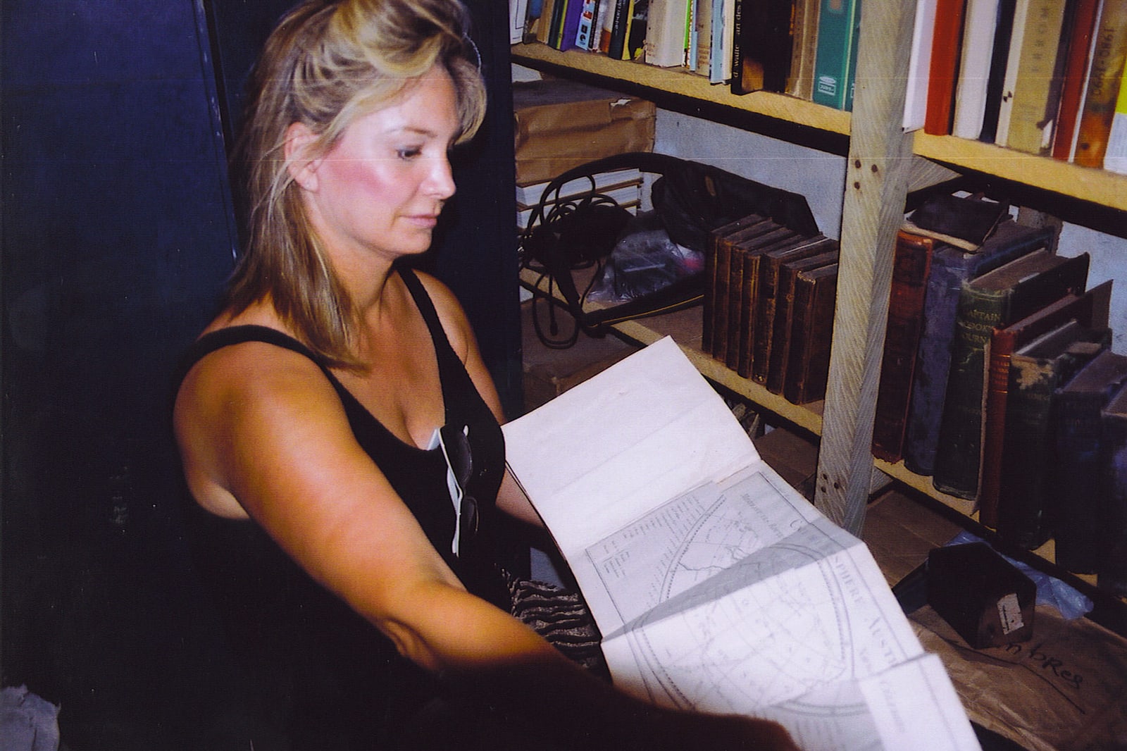 Joni Rogers-Kante holding an open atlas beside shelves of books.